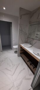 Salle de bain moderne en cours de finition, carrelage marbre blanc, double vasque, WC suspendu et porte coulissante.