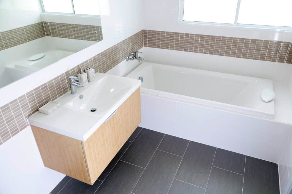 Salle Bain Design : Vasque, Baignoire et Carrelage Moderne Salle de bain moderne avec vasque en bois clair, baignoire intégrée, carrelage mural blanc et mosaïque marron, sol gris foncé.