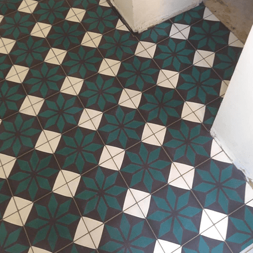 Carreaux de Ciment Étoilés Vert Émeraude et Blanc Sol en carreaux de ciment anciens, motif étoilé géométrique en vert émeraude, blanc cassé et gris foncé, près d'un mur blanc.