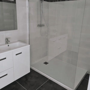 Salle de bain moderne avec meuble-lavabo blanc et grande douche à l'italienne carrelée de gris clair sur sol noir.