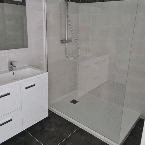 Douche à l'italienne moderne et meuble-lavabo blanc Salle de bain moderne avec meuble-lavabo blanc et grande douche à l'italienne carrelée de gris clair sur sol noir.