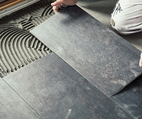 Pose de carrelage foncé, revêtement de sol en cours Pose de grandes dalles de carrelage gris foncé texturé sur mortier frais, créant un sol moderne.